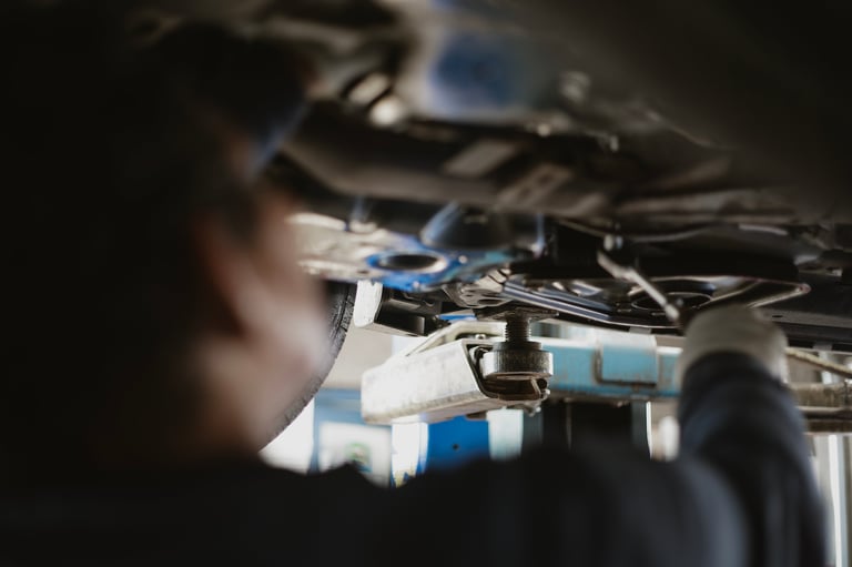 A mechanic is focused on repairing a vehicle from underneath, with various tools visible around. The setting appears to be a professional repair shop.